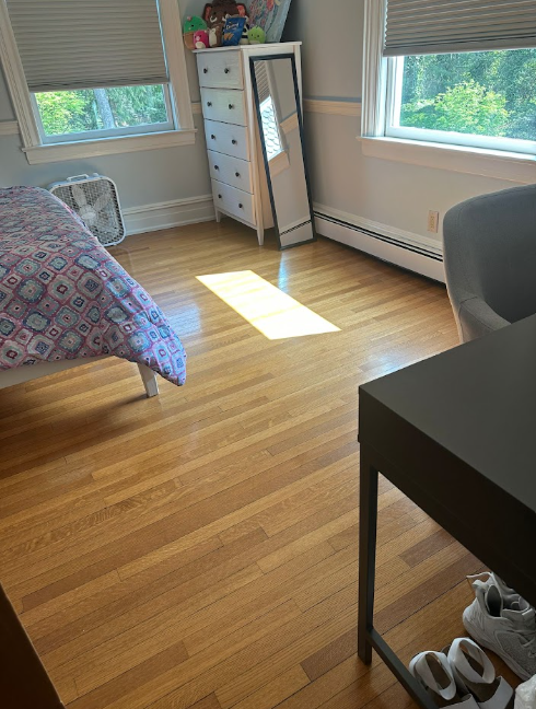 Clean bedroom featuring a streak-free full-length mirror beside a white dresser and sunlit hardwood floor